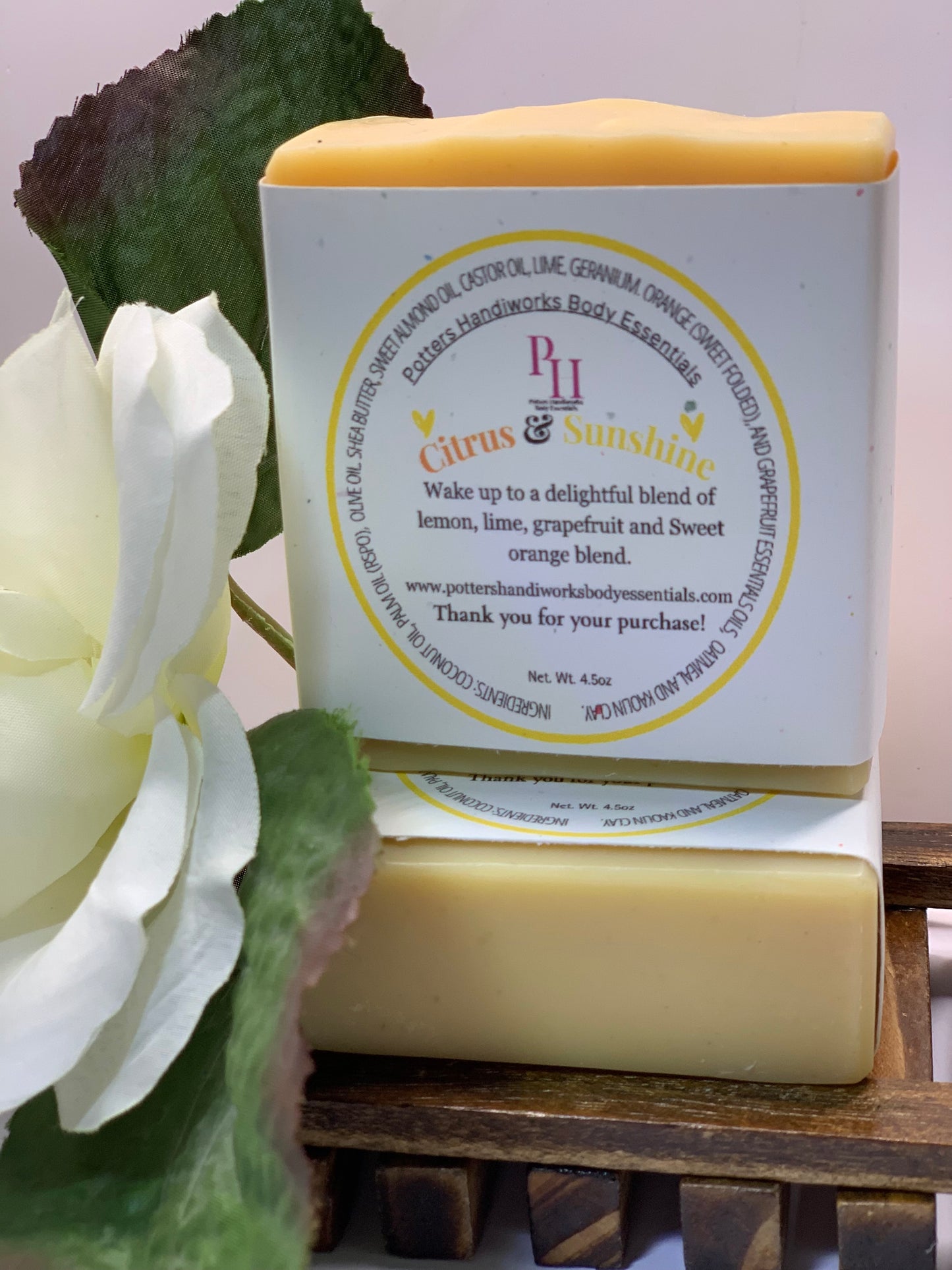 Bar of soap with a label featuring 'P&H' branding, next to a white flower on a wooden surface.