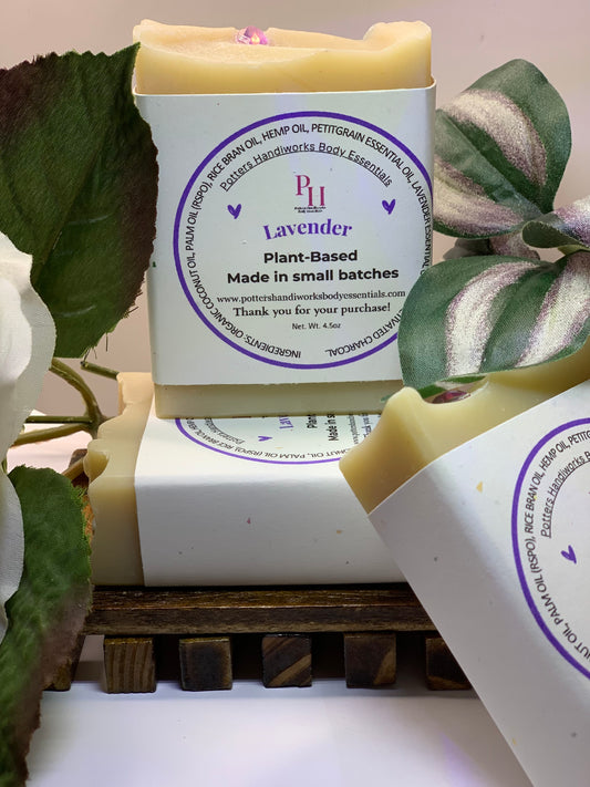 Lavender soap bars with visible branding on a wooden block surrounded by green leaves.