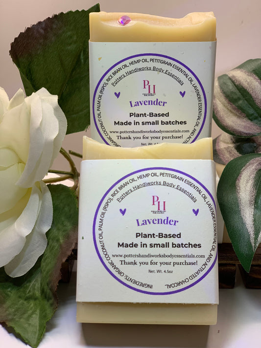 Two lavender soap bars with purple labels on a white surface with green leaves in the background.