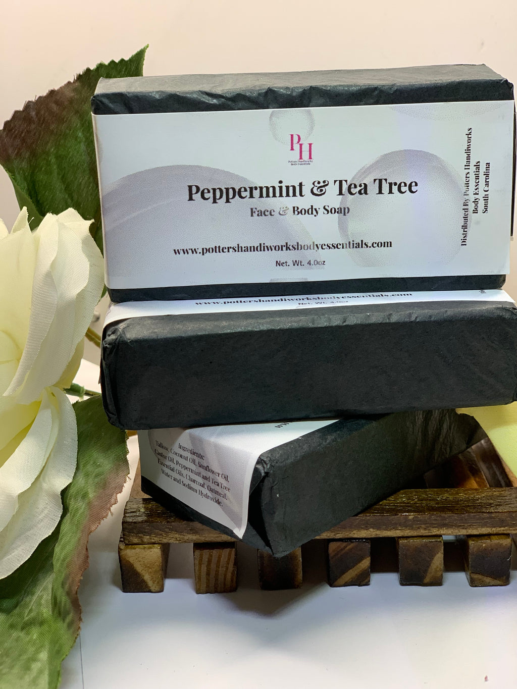 Two bars of peppermint and tea tree soap on a wooden stand with a white flower in the background.